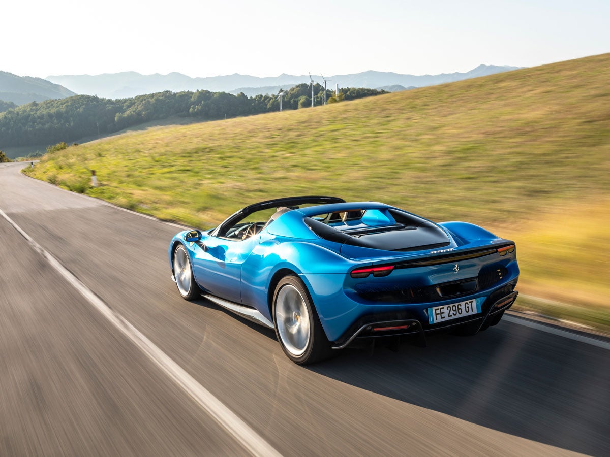 A bright blue convertible sports car drives on a winding road with green hills in the background.