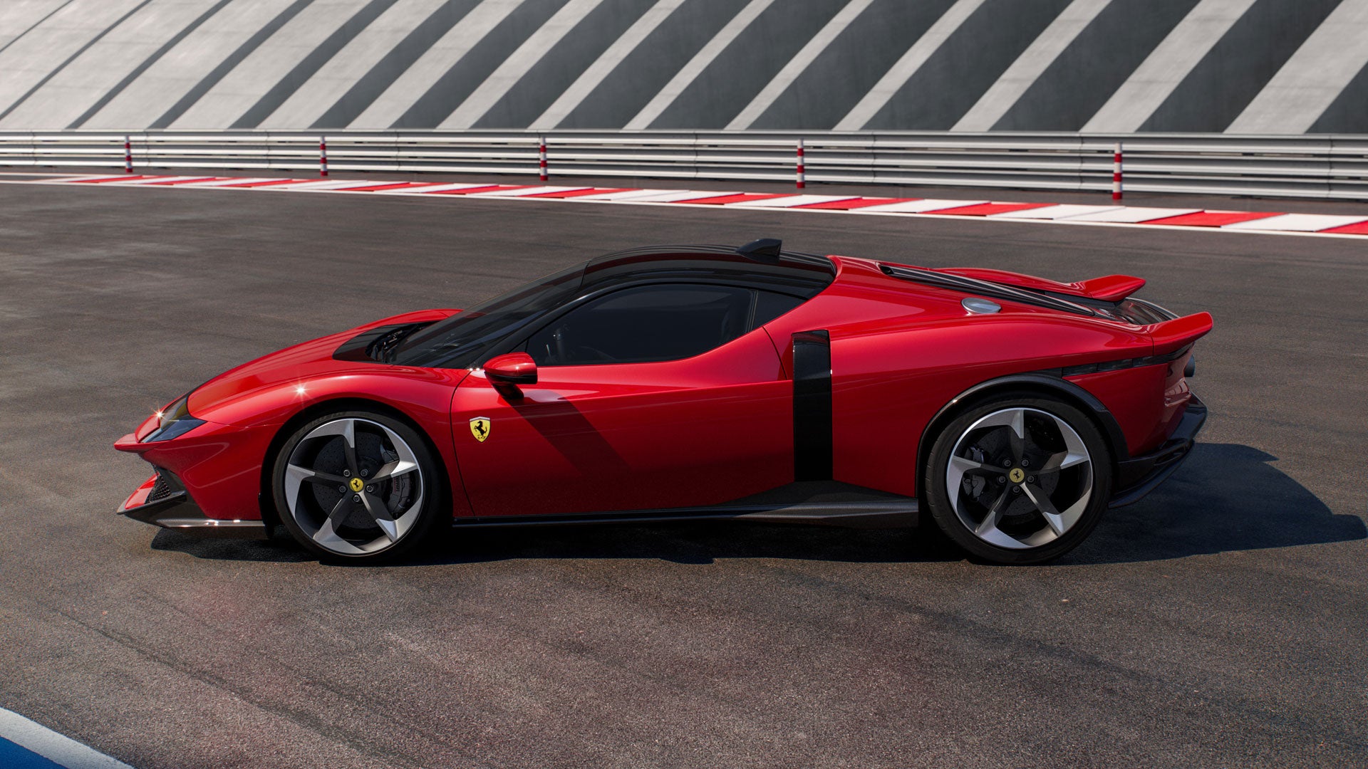 Side view of a red Ferrari supercar with black roof and accents, parked on a racetrack.