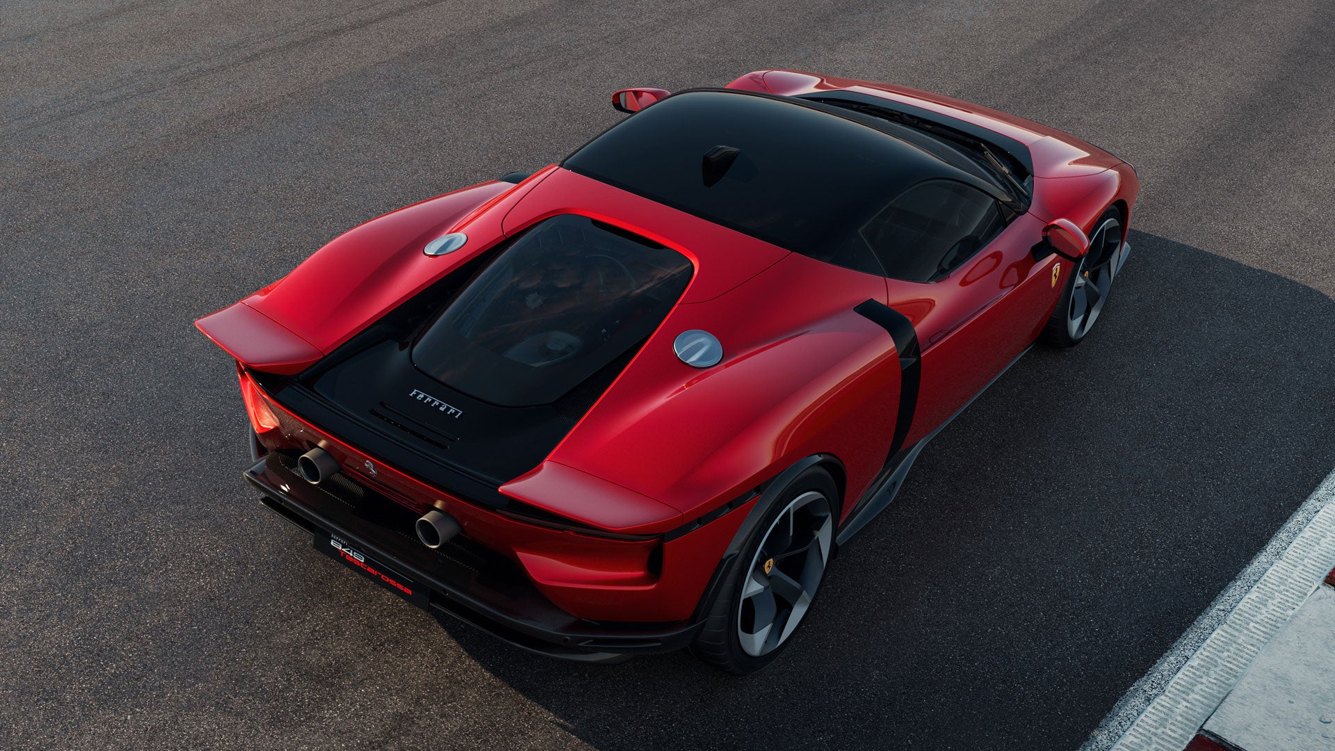 Overhead view of a glossy red sports car with a black roof and engine cover, parked on asphalt.